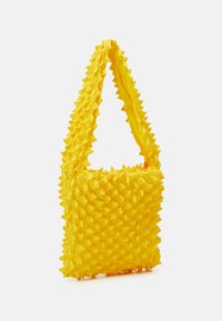 Yellow tote bag with a textured, spiked exterior. Made from flexible material, it features a single strap and a rectangular shape.