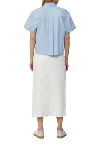 Camicetta azzurro chiaro a maniche corte con piega sul retro, abbinata a una gonna di jeans bianca che arriva a metà polpaccio e a delle scarpe da ginnastica bianche con suola beige.