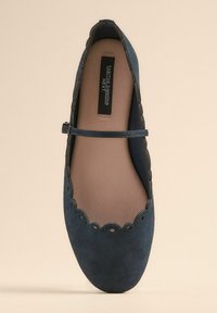 Blaue Wildleder-Ballerinas mit gewelltem Rand, Knöchelriemen und glattem Innenfutter. Die Sohle ist rund und das Design ist minimalistisch.