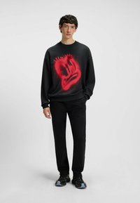 Czarna bluza z dużą czerwoną grafiką w stylu graffiti na przodzie, luźny krój, okrągły dekolt, zestawiona z czarnymi spodniami i trampkami.