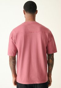 T-shirt med kort ärm och avslappnad passform i dammig rosenfärg, tillverkad av mjukt bomull. Har en rak fåll och synliga sömmar på baksidan.