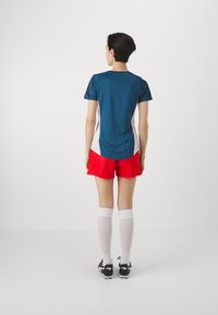 Spordirõivad, mis sisaldavad türkiissinist lühihelist toppi, punaseid lühikesi pükse, valgeid sokke ja musti jalgpallijalatseid, mõeldud sportimiseks.