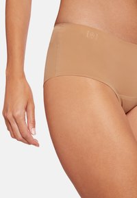 Beige sømløst hipster undertøj med en glat tekstur og diskret logodetalje på taljebåndet, med standard pasform og blød elastik.