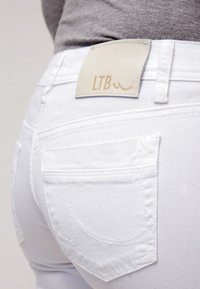 Jeans de mezclilla blanca con una textura suave y bolsillos traseros. Presenta una etiqueta de cuero beige con la inscripción "LTB" en la cintura.