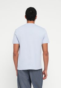 Jasnoniebieski t-shirt z krótkim rękawem i okrągłym dekoltem, gładka faktura, dopasowany krój oraz gładki tył. W zestawieniu z średnioniebieskimi spodniami.