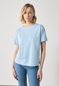 Lyse blå crew-neck T-skjorte laget av glatt bomullsblanding, med korte ermer og løs passform, sammen med blå jeans med rett ben.