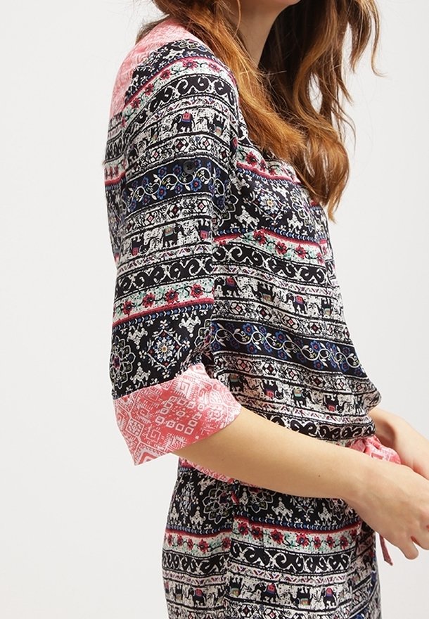 Blouse à motifs noir et rose avec des manches courtes. Présente des designs élaborés avec des éléphants et des motifs floraux. Tissu léger.