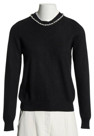 Pull noir à manches longues avec détail de perles autour de l'encolure ronde, présenté sur un buste de mannequin blanc avec pantalon blanc.