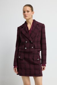 Bordeaux tweed pak met een dubbelknopige jas met twee zakken en een bijpassende rok. Accenten van zilveren knopen en een geruit patroon.