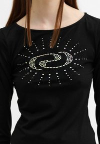 Schwarzes Langarmshirt mit einem zentralen Design aus schillernden Strasssteinen, die ein spiralförmiges Muster mit strahlenden Linien bilden.