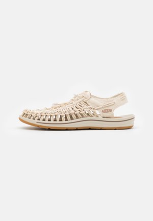 Sandal beige chiaro con design superiore intrecciato, schiena aperta, suola sagomata e dettagli testurizzati. Presenta una suola in gomma leggera per la trazione.