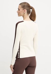 Top a maniche lunghe bianco a costine con accenti marroni sulle spalle e sui lati, con un dettaglio logo all'orlo. Tessuto liscio, design aderente.