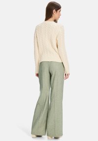 Cream cable-knit sweater with a round neck, paired with light green flared trousers. The outfit features textured materials and neutral tones.