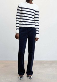 Sweter w paski w białym i granatowym kolorze, zestawiony z granatowymi spodniami z sztruksu. Modelka nosi srebrne szpilki w kształcie spiczastym. Gładka tekstura i dopasowany krój.