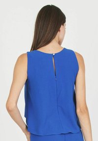 Top azul sin mangas con escote redondeado, abertura tipo ojal en la parte posterior y una tela suave con un ajuste ligeramente holgado.