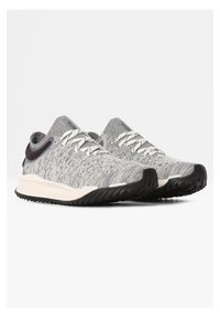 Šedé pletené sportovní boty s bílými tkaničkami, zaoblenou špičkou a texturovanou podrážkou. Mají tmavý akcent na patě a nízký střih.