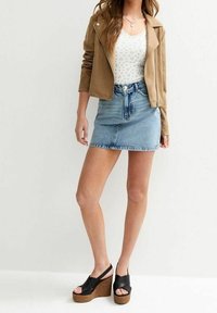 Béžová bunda z umělé kůže, bílý květinový top, modrá džínová minisukně a černé sandály na klínu s texturovanou korkovou podrážkou.