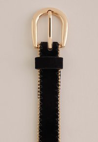 Črni žametni pas z zlato okroglim sponkom in zlatim obrobnim okrasjem iz kroglic ob robovih, prikazan na nevtralnem ozadju.