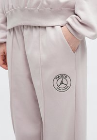 Lyserøde sweatpants med en afslappet pasform, der har et sort rundt logo med teksten "PARIS" og "SAINT-GERMAIN" samt en detalje med sidelommer.