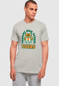 Graues Baumwoll-T-Shirt mit einem großen orangenen Tiger-Graphic, darüber in Grün "HAWKINS HIGH SCHOOL" und darunter in Orange "TIGERS".