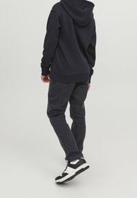 Marineblaues Hoodie mit einer Tasche, kombiniert mit dunkelgrauen Jeans. Die Schuhe sind schwarz-weiße Sneaker mit einer strukturierten Sohle.