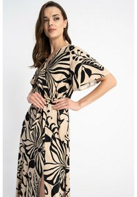 Beżowa maxi sukienka w czarne kwiatowe wzory, z krótkimi rękawami i wężem w talii, gładki materiał z luźnym krojem.