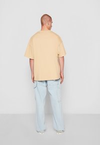 Beige oversized bomulls T-skjorte med korte ermer, sammen med lyseblå vide denimjeans med cargo-lommer og subtil logo-detalj.