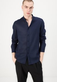 Camicia blu navy con bottoni, realizzata in tessuto leggero, dal taglio slim, con maniche lunghe e una texture sottile. Nessun motivo o dettaglio visibile.