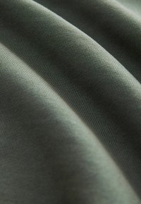Olívovo zelená ľahká tkanina s hladkým povrchom, predstavujúca jemný pružný materiál a viditeľné tkané vzory, ukazujúca mäkké, splývavé záhyby.