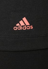Materiale atletico nero con una texture liscia. Presenta un logo Adidas rosa e dettagli delle cuciture visibili.