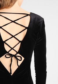 Svart sammetklänning med långa ärmar och djup V-back med en korslagd snörning och en knytning på den nedre ryggen.
