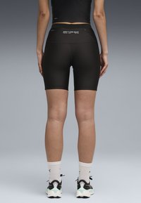 Shorts de vélo noirs taille haute en matière extensible, dotés d'une poche zippée et d'un texte blanc "NE REGARDEZ PAS EN ARRIÈRE" sur la ceinture arrière.