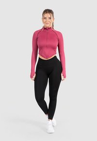 Fitted, cropped zip-up jacket in pink, paired with high-waisted black leggings. Smooth texture, long sleeves, and thumbhole openings on the jacket.