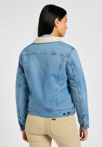 Chaqueta de denim en azul claro con un cuello de borreguito color crema, con un diseño ajustado y puños abotonados. Detalles de costura limpios y clásicos visibles.