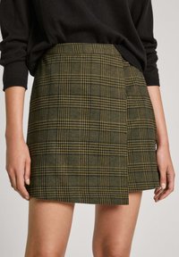 Green plaid skirt with yellow accents, featuring a tailored fit and a slightly asymmetrical hemline, made from textured fabric.
