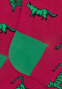 Calzini colorati con sfondo rosa e motivi di dinosauri verdi. Il design include un bordo superiore verde pieno e una texture liscia.