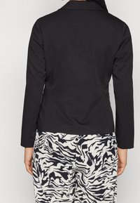 Svart skräddarsydd kavaj, enknäppt med notch-krage, långa ärmar; tillsammans med mönstrade vita och svarta vida byxor.