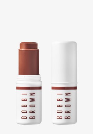 Stick crema marrone Bobbi Brown con tappo bianco accanto a tappo bianco chiuso abbinato su sfondo semplice.