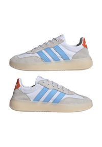 Par hvide sneakers med lyseblå striber, grå ruskindsoverlays, gennemsigtige beige såler og orange hælflapper vist fra siden.