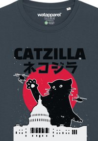 Donkergrijze t-shirt met een grafiek van een zwarte kat tegen een rode cirkel, met silhouetten van een gebouw en helikopters, en vette tekst erboven.