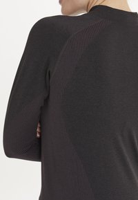 Langärmliges Sportoberteil in Dunkelgrau mit gerippten Seitenpanelen und glatter Textur, entworfen für Flexibilität und Komfort.