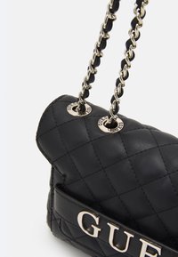 Czarna pikowana torebka na ramię z metalowymi łańcuszkami i akcentem logo. Wykonana ze skóry, charakteryzuje się usztywnionym kształtem i gładką fakturą.