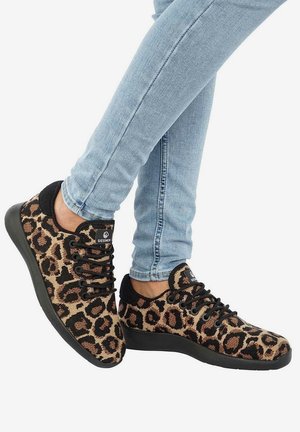Paire de baskets imprimé léopard avec semelles et lacets noirs, portées avec un jean skinny bleu clair, pieds croisés aux chevilles.