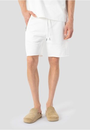 Witte katoenen shorts met een elastische tailleband, trekkoord en een zijritszak, gecombineerd met beige instapschoenen.