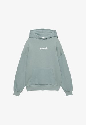 Light teal sweatshirt with a hood, oversized fit, front pocket, and "Dramatic" printed in white. Soft texture, ribbed cuffs, and hem.