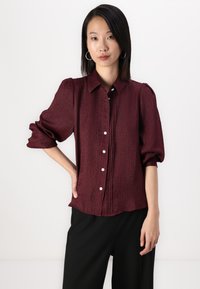 Burgundy textured shirt with a collar, puffed sleeves, and button-front design. Features decorative buttons and a relaxed fit.