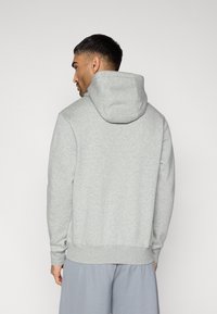 Sweat à capuche gris en coton avec une grande capuche, poignets et ourlet côtelés, porté avec un short gris. Le tissu semble doux et confortable.