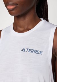 Top bianco senza maniche, realizzato in tessuto leggero e testurizzato, con un logo navy "TERREX" sul petto. Design semplice con scollatura rotonda.