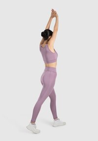 Top corto deportivo de color morado claro y leggings de cintura alta, con una textura suave y diseño ajustado, combinados con zapatillas deportivas blancas.