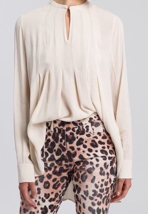 Kremowa bluzka z długim rękawem, plisami i dekoltem w kształcie klucza, w połączeniu z wysokim stanem spodni w panterkę.
